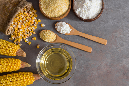 Corn flour, starch in wooden bowl, spoon with dried corn groats, kernels on rustic table. Corn cooking oil and corn ingredients