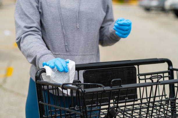 Customer Wipes Down Handles of Grocery Cart Shopper wearing gloves to prevent the coronavirus covid-19 uses a disinfecting wipe to clean the handle of a shopping cart. medium shot stock pictures, royalty-free photos & images