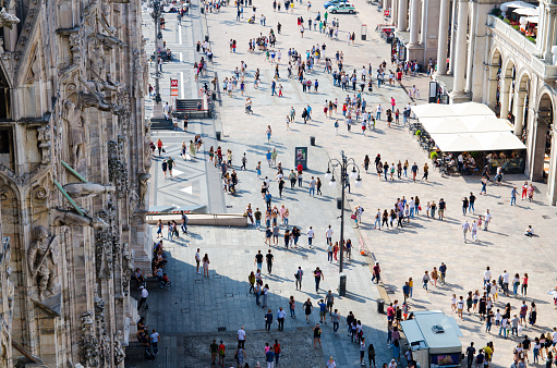 Milan, Italy, September 9, 2018: Crowd of small figures many people are walking on Piazza del Duomo square near Gallery Vittorio Emanuele II in historical city centre, top view from Milano cathedral