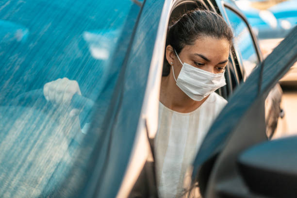 woman getting into her car with a protection mask - illness mask pollution car imagens e fotografias de stock