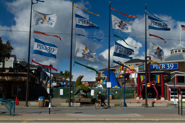 San Francisco, California - March 25th, 2020: A mask covered bicyclist is riding by the closed down Pier 39 at Fisherman's Wharf during the Covid-19 pandemic