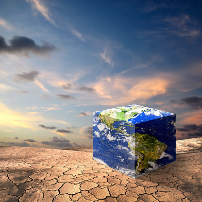 Conceptual image of cube shaped world map dry cracked landscape over dusk sky. NASA world map image layered and used; https://apod.nasa.gov/apod/image/0304/bluemarble2k_big.jpg