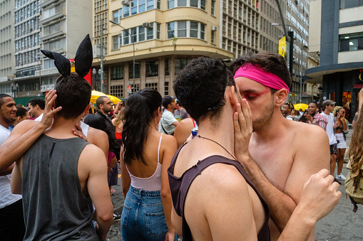 Sao Paulo, Brazil - February 29, 2020: Male couples kiss each other while others celebrate Sao Paulo’s carnival at a “bloco” street party along Avenida Ipiranga.