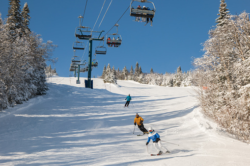 view of skiers climb the ski lift up the hill with snow covered mountains. Ski chairlift climb above the ski slope