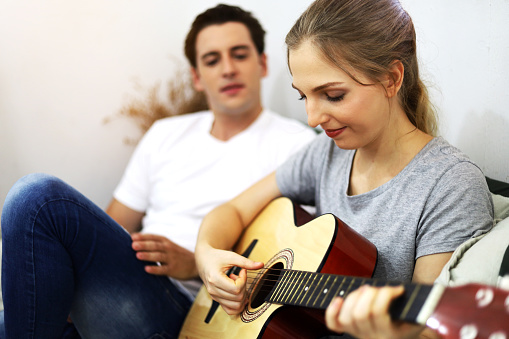 Young couple lover playing acoustic guitar on bedroom at home.