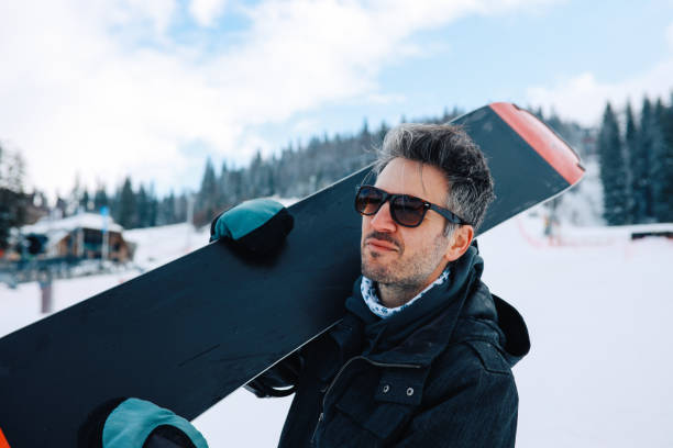 istock Mid aged man taking his snowboard to the mountain top 1214835876