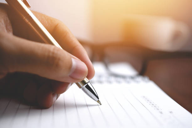 istock Pen writing on a notebook, Close-up men hand holding silver pen writing letter on a notebook 1214838447