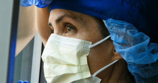 Sad, sick, overworked, female health care worker Young Sad, sick, overworked, female mature health care worker looking through a window mediterranean ethnicity stock pictures, royalty-free photos & images