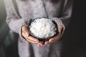 Asian women holding cooked jasmine rice bowl. Wearing a gray sweater.
