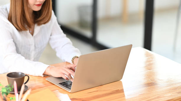 istock Cropped image of beautiful woman working as secretary typing on computer laptop while sitting at the wooden working desk over comfortable workplace as background. 1214851567