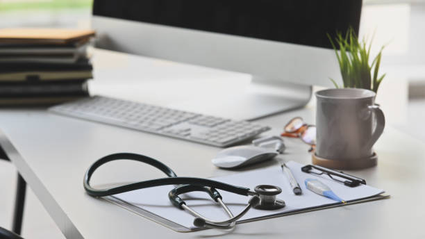istock Stethoscope putting on white working desk with Coffee cup, Potted plant, Clipboard, Wireless mouse and keyboard, Stack of books, Doctor workspace in medical centre. 1214851579