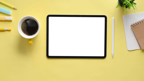 istock Top view image of cropped black computer tablet with white blank screen, coffee cup, pen, notebook, potted plant putting together on working desk. Orderly workplace concept. 1214851583