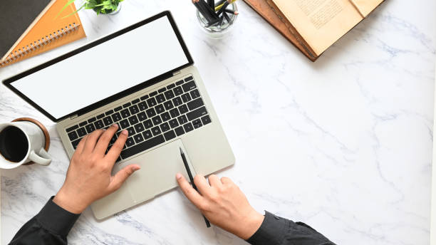 istock Top view image of businessman's hands using a computer tablet with white blank screen that putting on marble texture table with coffee cup, notebook, books, potted plant and pencil holder. 1214851637