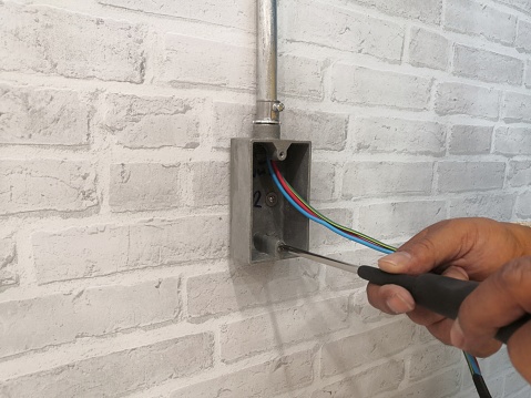 Electrician installing F.S. BOX for electrical system work on gray brick wall.Technician installation electrical system work.