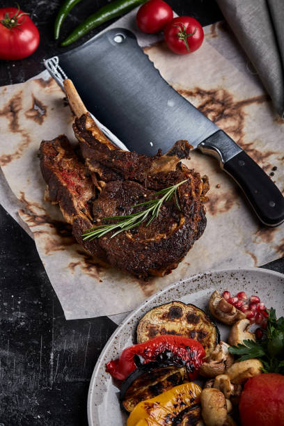istock Tomahawk steak with vegetables and a knife on the table. Grilled meat with grilled vegetables and fresh vegetables on the table 1214854893