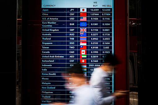 People walk in front of a foreign currency exchange monitor .