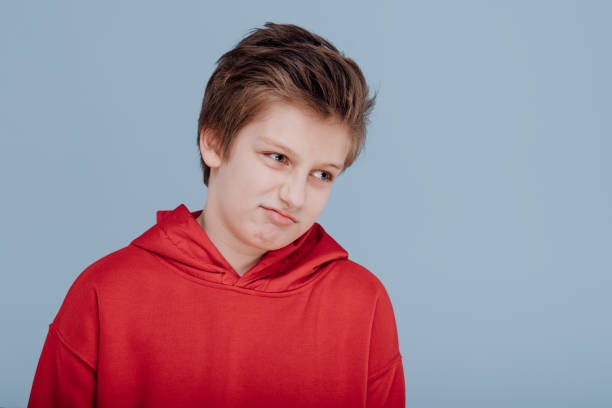 istock sad boy in red sweatshirt, isolated on blue background, copy space 1214857299