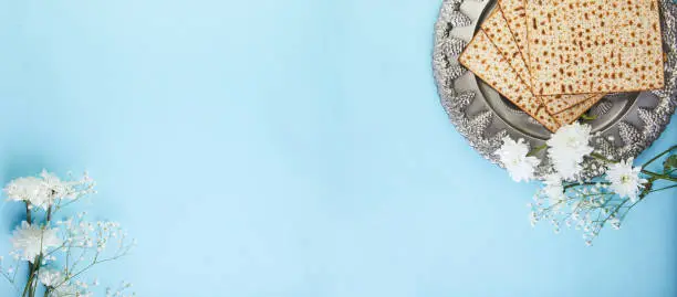 Pesah celebration concept - jewish Passover holiday Background matzo and seder plate with white flowers on a blue background. View from above. Flat lay banner.