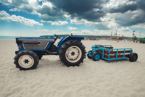 A green tractor with a motor and caterpillars on the sandy beach of the Baltic Sea helps to pull a fishing boat ashore