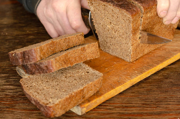 istock Male hands slicing fresh bread on wood table 1214859848