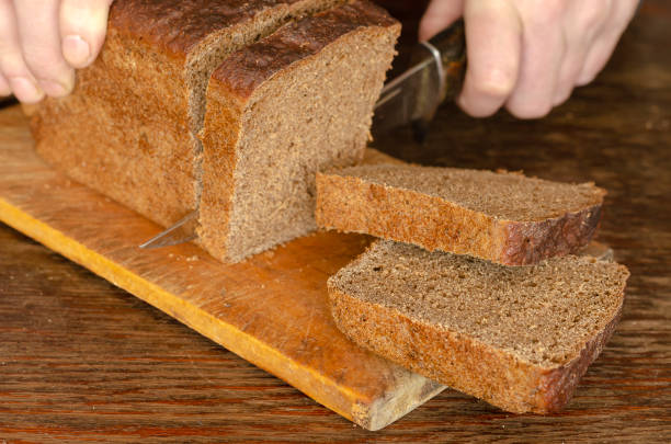 istock Male hands slicing fresh bread on wood table 1214860364