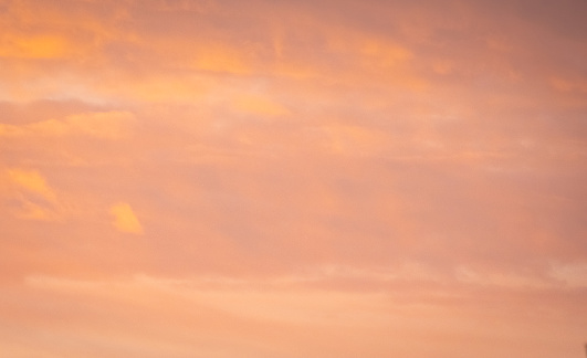 An early morning sunrise fills the sky with a peachy orange light. The clouds give it soft texture and depth.