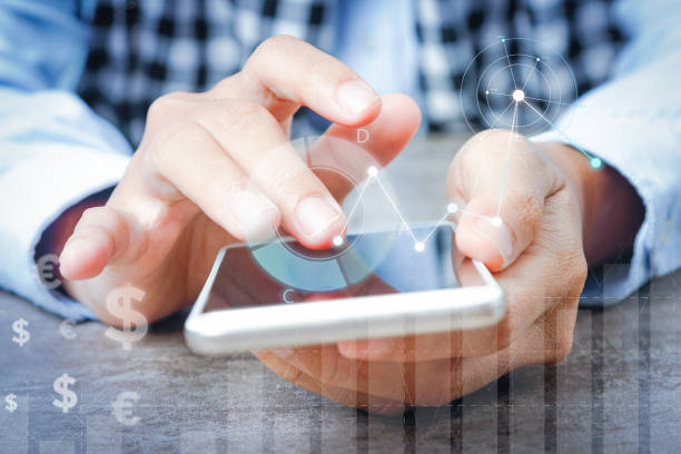 istock Woman using smartphone at table with financial analysis graphs 1214867499