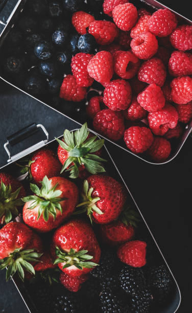 istock Flat-lay of fresh berries in lunchboxes over dark background 1214868572