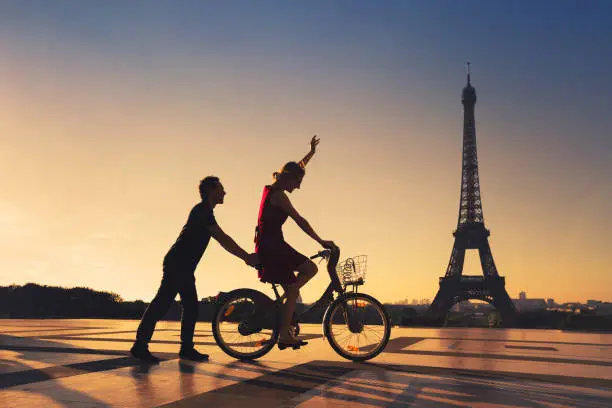 Photo of happy couple having fun in Paris riding bicycle near Eiffel tower