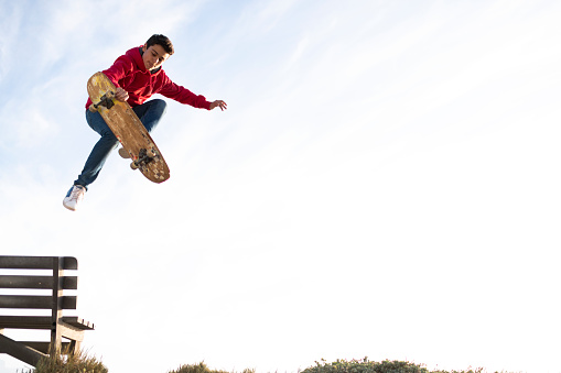 Wide shot teenage skateboarder jumps off bench holds board in skating trick