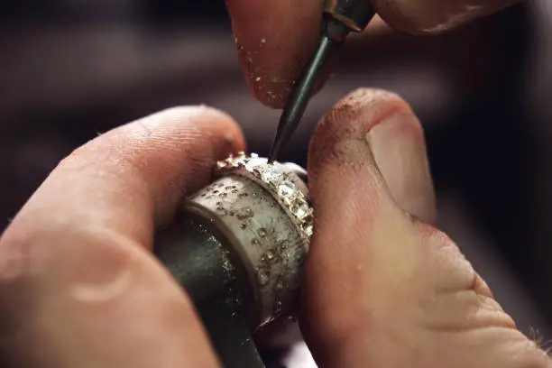 Photo of Close up of a goldsmith's hand making a gold or silver ring or a diamond using goldsmith's tools. For this work it takes precision and patience