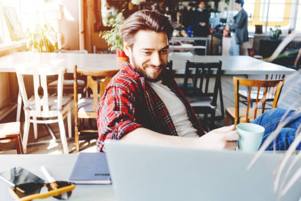 istock Young stubbled man working with laptop in big bright office space. Comfortly sitting and smiling at the table 1214876128