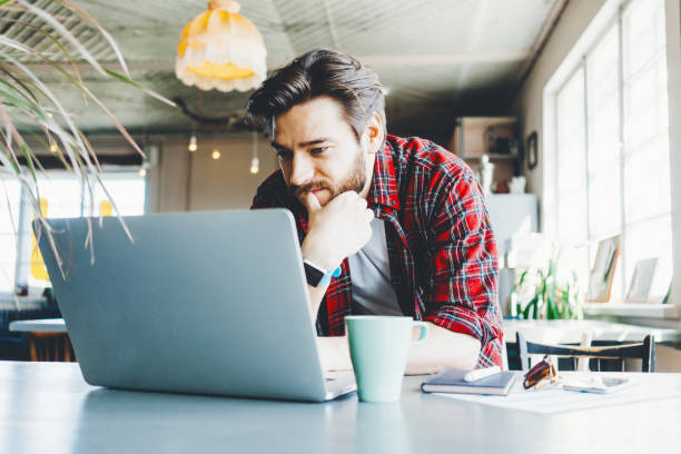 istock Young stubbled man working with laptop in big bright office space. Thinking about new plan 1214876198
