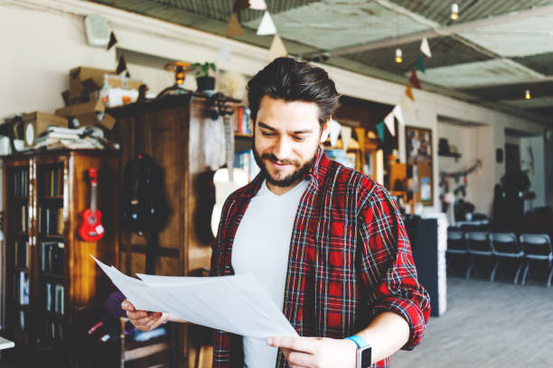 istock Young stubbled man reading paper stats and graphs in big bright office space 1214876504