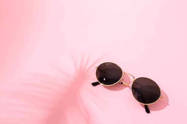 istock round shape black sunglasses on pink background with tropical leaf shadow 1214884327