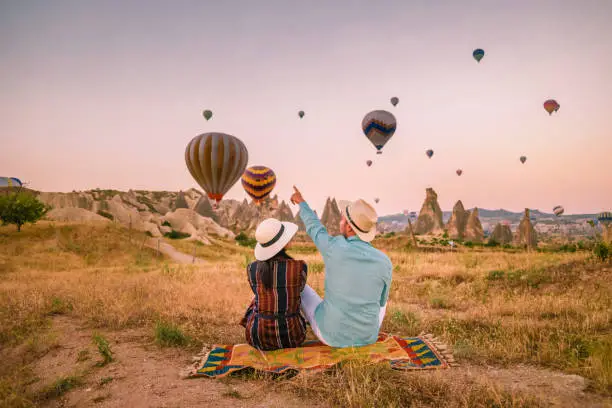 Photo of Cappadocia Turkey during sunrise, couple mid age men and woman on vacation in the hills of Goreme Capadocia Turkey, men and woman looking sunrsise with hot air balloons in Cappadocia