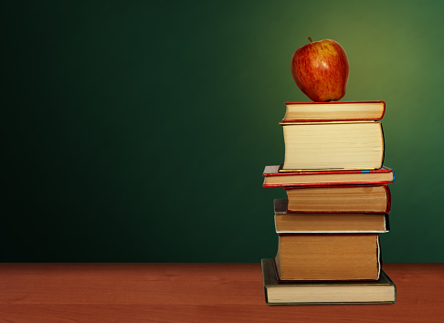 Back to school, pile of books and red apple with empty green school board background, education concept