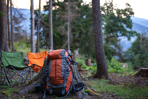 Camping in a mountain forest: Hiking chairs and a large Hiking backpack on the ground. A place to rest with a beautiful mountain panorama