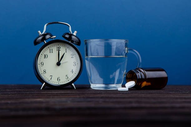 istock It's time to take a daily dose. Clock and pills on a wooden table. blue background 1214894513