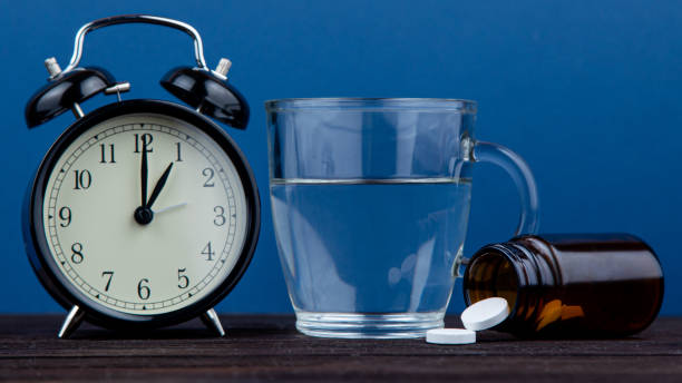istock It's time to take a daily dose. Clock and pills on a wooden table. blue background 1214894868