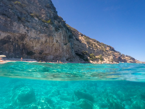 Cala dei Gabbiani, Italy - September 13, 2017: View over and under water surface, rocks and blue sky, mediterranean sea, split by waterline at Cala dei Gabbiani, Sardinia, Italy