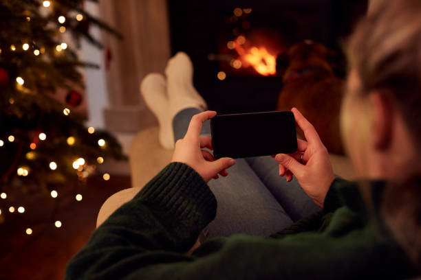 istock Woman At Home Using Mobile Phone With Blank Screen At Christmas 1214901138
