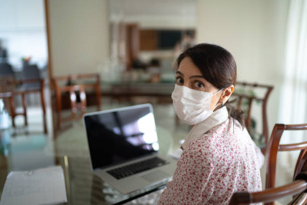 retrato de mulher de negócios sênior trabalhando em casa usando máscara de proteção - looking at camera senior women laptop only women - fotografias e filmes do acervo