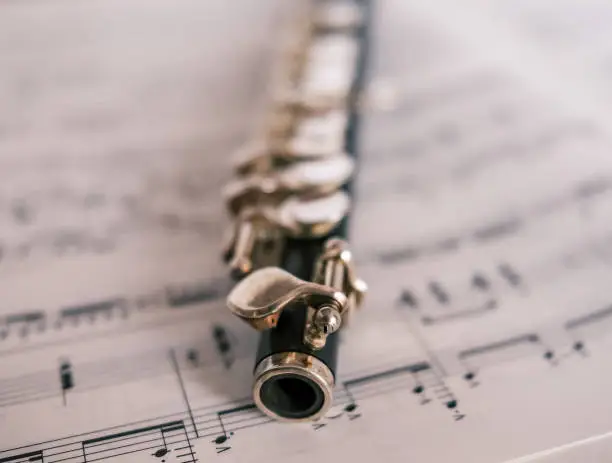 Close up and selective focus of a classic wooden flute on a background of unidentifiable sheet music