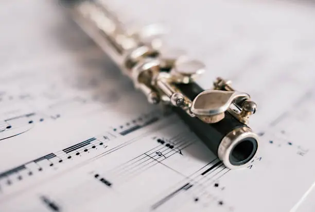 Close up and selective focus on a classic wooden flute on a background of unidentifiable sheet music