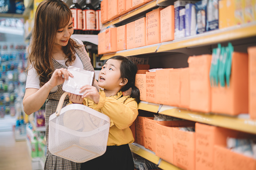 an asian chinese mother and daughter shopping in a pharmacy store and playing with the shopping basket bonding time