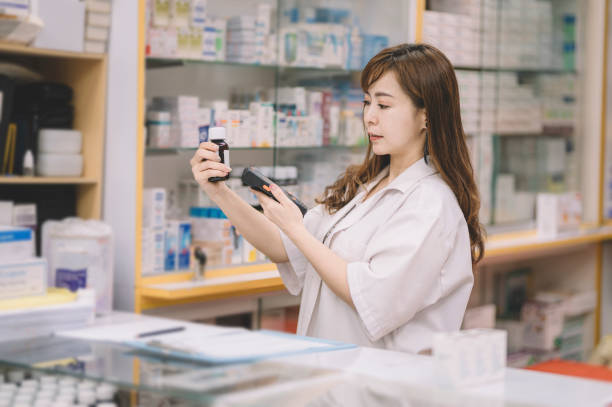 an asian chinese female pharmacist scanning on a bottle of pills for the pricing details at the cashier counter an asian chinese female pharmacist scanning on a bottle of pills for the pricing details at the cashier counter labeling photos stock pictures, royalty-free photos & images