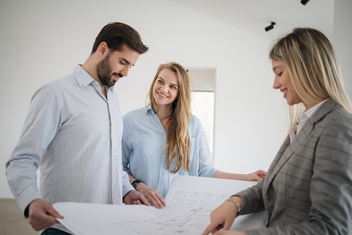 Couple Meeting with architect or real estate agent presenting new house design and blue prints. They are examining blueprint together and enjoy idea of new home.