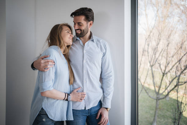 istock Happy young couple in bedroom looking out sunny window 1214913507