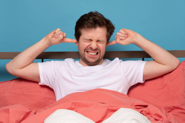 istock Young man plugging ears with fingers and winking sitting at bed 1214913932